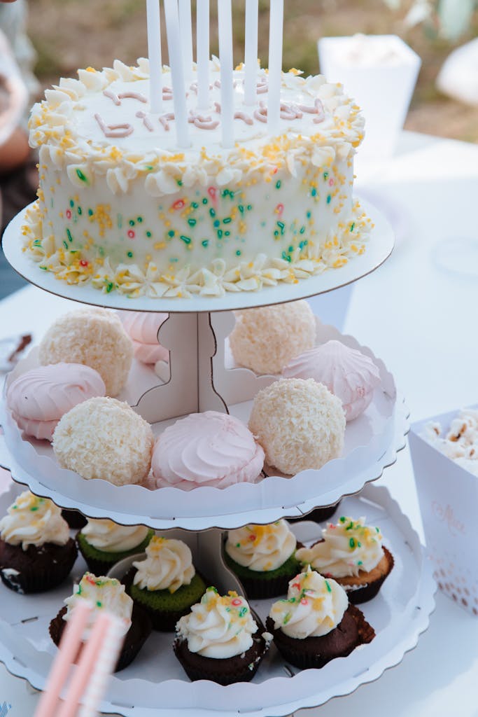 Festive display of birthday cake and cupcakes with sprinkles on a tiered stand, perfect for celebrations.