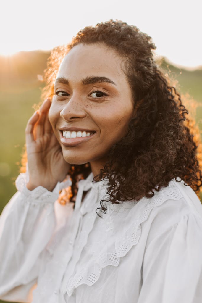 Portrait of a smiling woman outdoors with curly hair and freckles, enjoying the sunset.