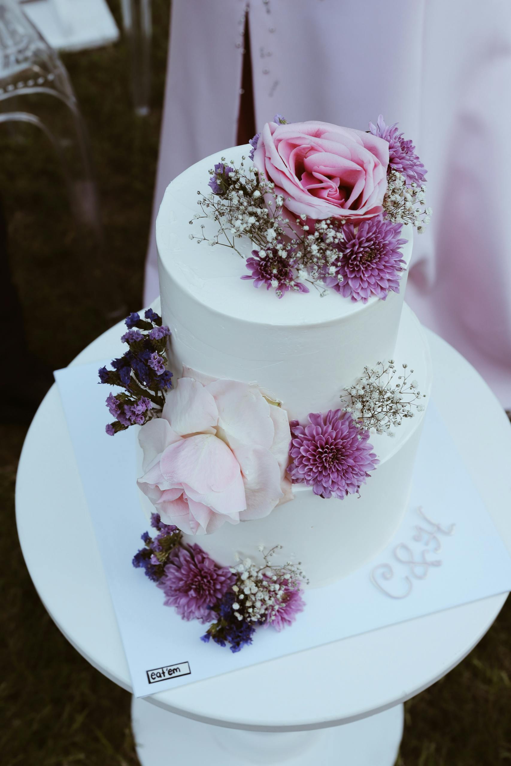 Two-tier white cake adorned with pink roses and purple chrysanthemums, perfect for weddings.