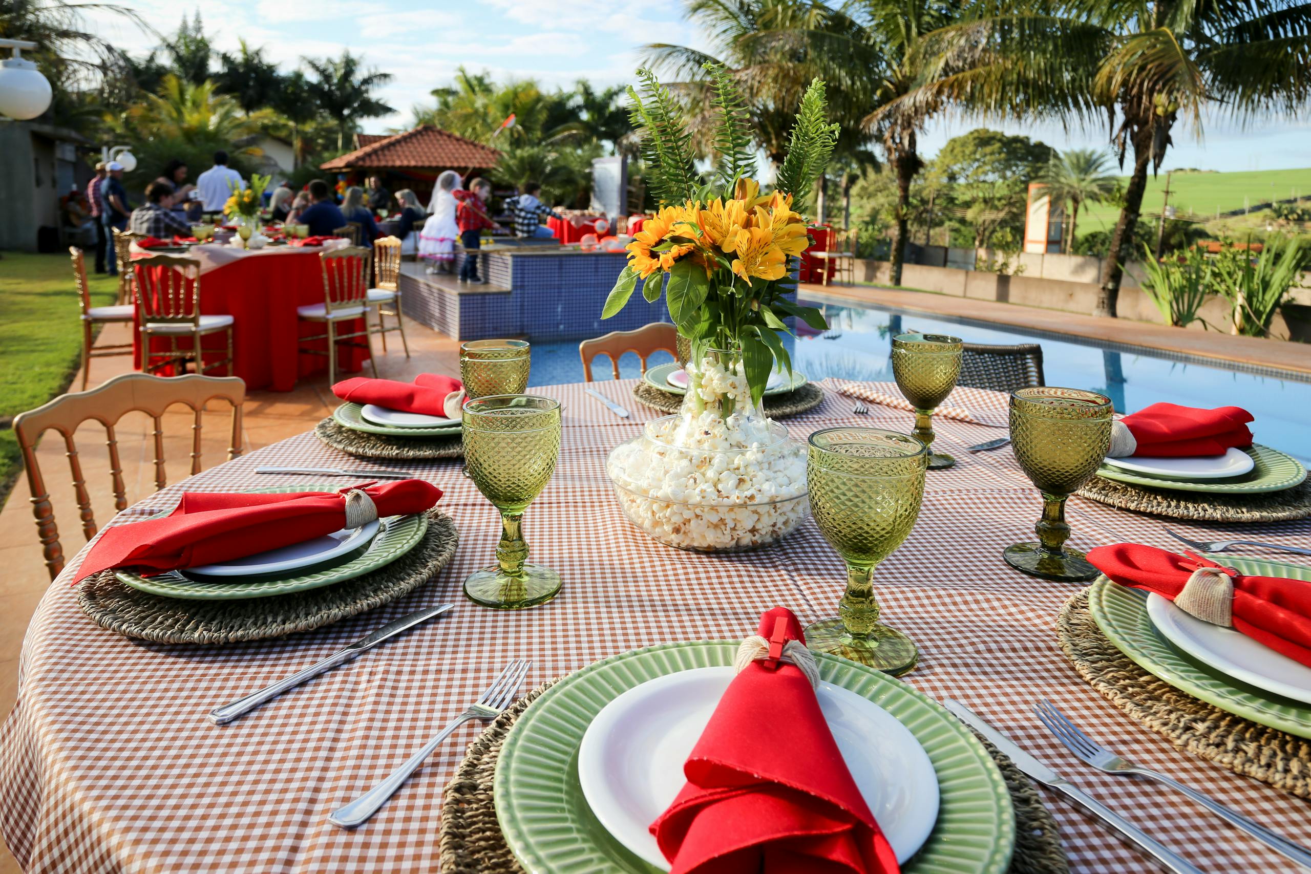 Vibrant outdoor dining setup with floral centerpiece by a pool, perfect for social gatherings.