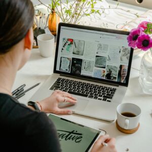 Woman in a creative workspace using a laptop and tablet for calligraphy. Artistic and tech-driven environment.