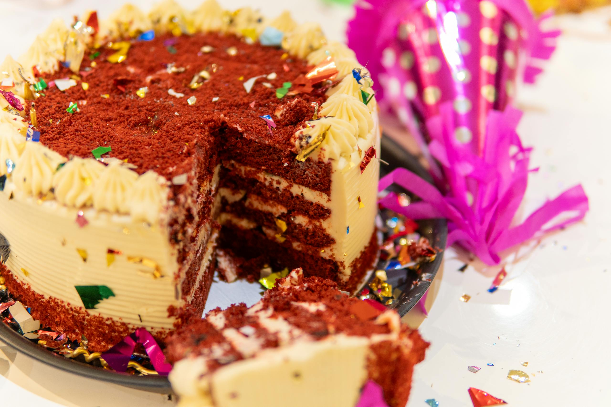 A vibrant red velvet cake with decorative confetti at a festive celebration.