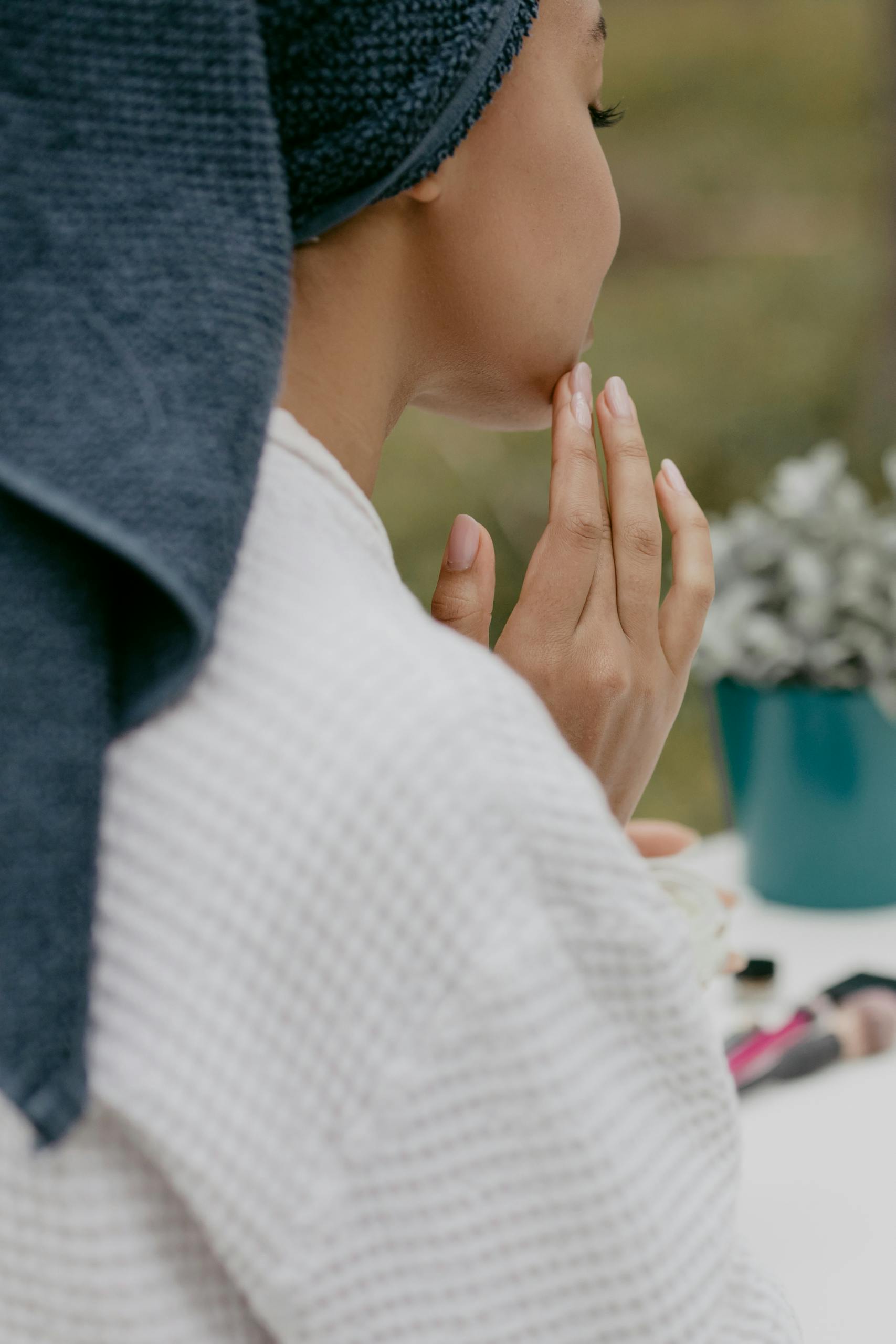 Back view of a woman applying facial cream, wearing a bath towel wrap, promoting healthy skin care.