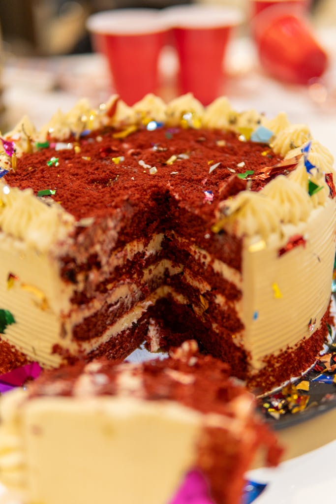 Close-up of a sliced red velvet birthday cake with confetti decorations.
