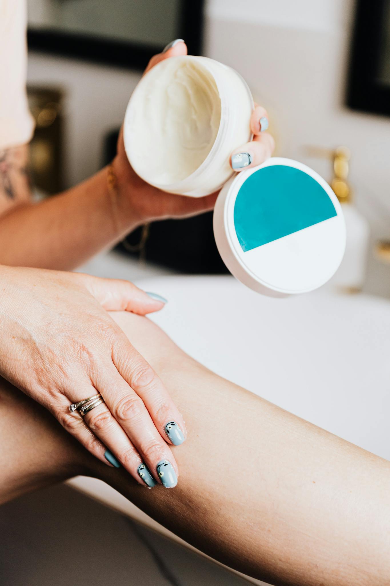 Close-up of a woman using lotion on her leg for skin care with manicured nails.