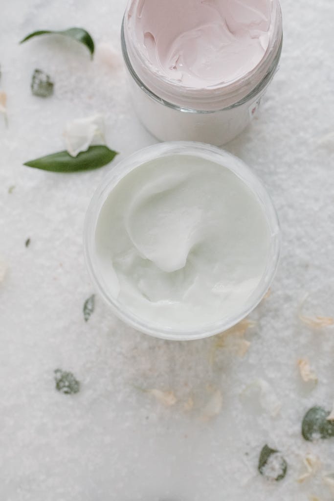 Top view of elegant skincare creams in glass jars with natural elements on a soft white background.