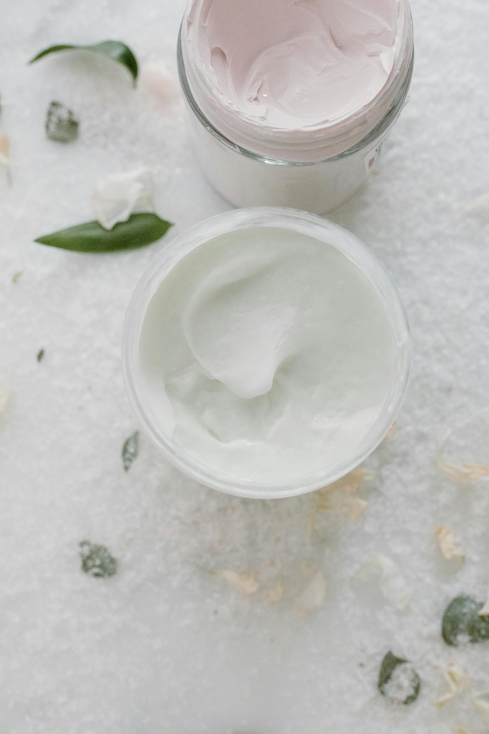 Top view of elegant skincare creams in glass jars with natural elements on a soft white background.